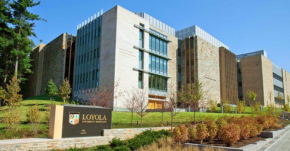 The tan-bricked facade of the Donnelly Science center as seen from the intersection of Cold Spring and Charles Street, with a Loyola sign in front